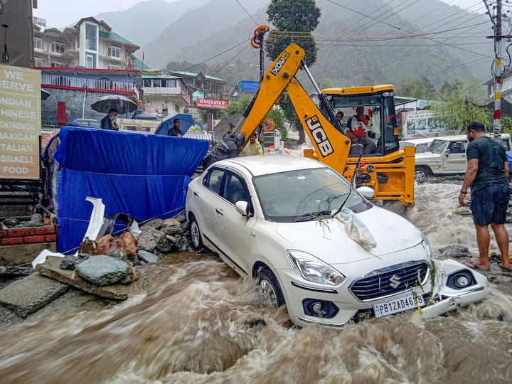 Dharamshala: Following the heavy downpour, the water level in the Manjhi River drastically rose damaging several shops and houses in the Chetru village of Dharamshala. An earthmover machine removes a vehicle stuck in flood water near Bhagsunag, as heavy rains lashed the area after a cloudburst in McLeodganj. (Image: PTI)