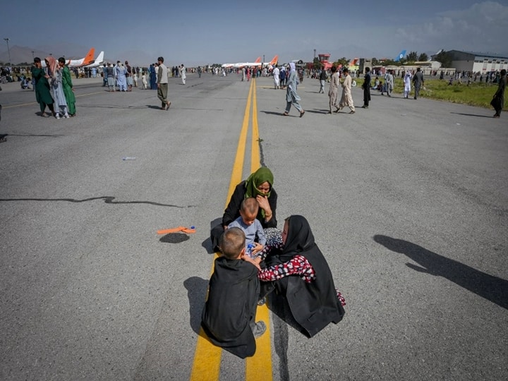 Afghan people sit along the tarmac as they wait to leave the Kabul airport in Kabul. (Wakil Kohsar / AFP)