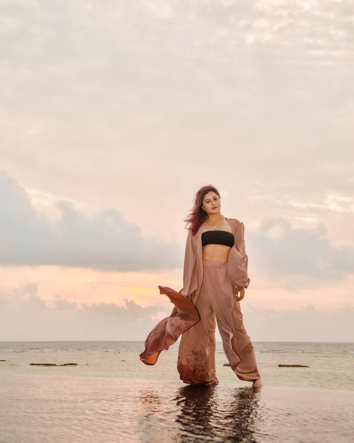 फोटो में रश्मि देसाई ब्राउन कलर का प्लाजो पैंट, ब्लैक ट्यूब टॉप और ब्राउन श्रग पहने हुए समुद्र किनारे खड़े होकर पोज देती हुई नजर आ रही हैं.