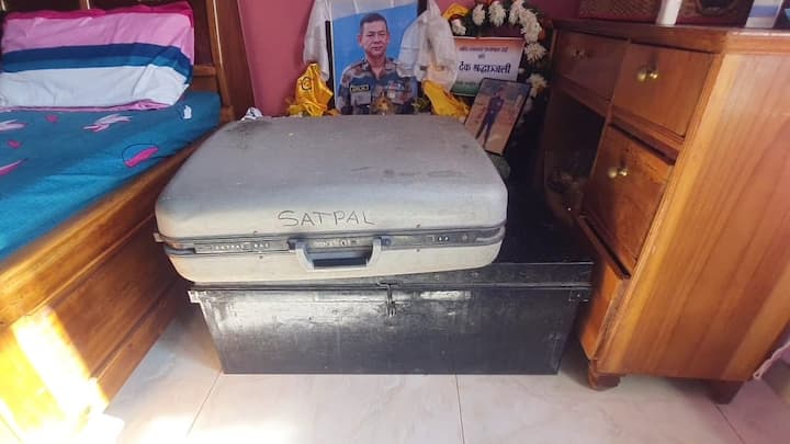 শোওয়ার ঘরে বিছানার পাশে রাখা সৎপালের সামগ্রী। স্যুটকেস, ট্রাঙ্ক, তাতে নাম লেখা সৎপালের।