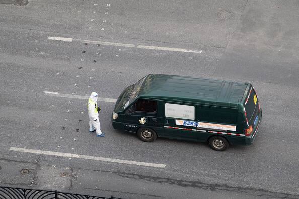 A government worker in PPE stops a van of China Post on an empty road in Shanghai, China Friday, April 01, 2022, the first day of the Covid-19 lockdown in the western part of the metropolis as public transport in most of the city has been suspended, while businesses considered non-essential, like restaurants and shopping malls, have also had to close. (Source: Getty Images)