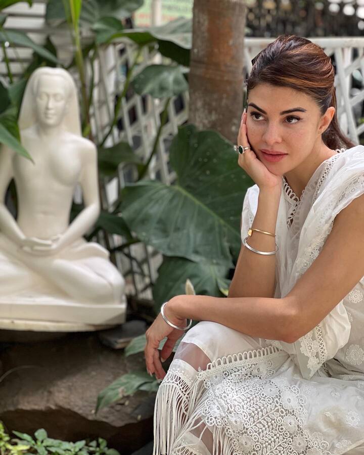 व्हाइट सूट पहने जैकलीन फर्नांडीज गार्डन एरिया में बैठे हुए इठलाती दिखीं हैं.