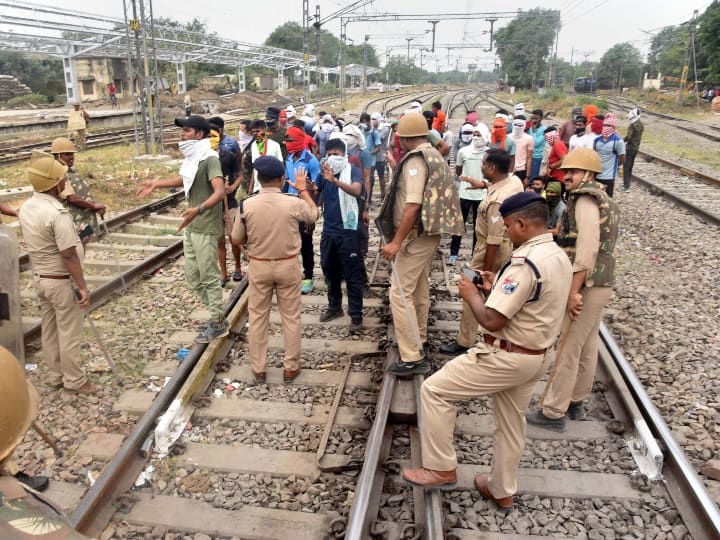 अग्निपथ योजन के विरोध में वाराणसी में रेलवे ट्रैक पर प्रदर्शनकारी छात्रों से बातचीत करते सुरक्षाकर्मी