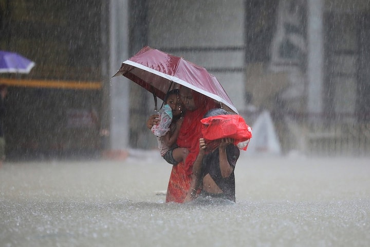 A woman with her child wades along a flooded street in Sylhet. Flooding has submerged roads and highways and isolated entire districts from the rest of the country. (Image Source: AFP)