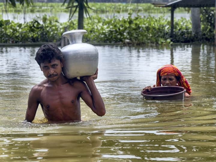 Villagers carry potable water in containers as they wade through a flooded area at Nilambazar village in Karimganj district. Water pouches and water purifying tablets are being distributed among the affected people, while temporary toilets have been set up in some camps. (Source: PTI)