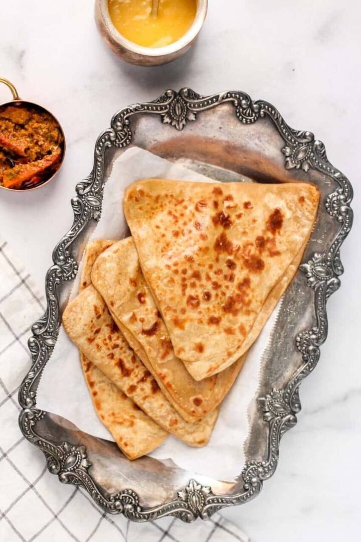 এবার রুটির থেকে মোটা করে পরোটা বেলে নিন। তারপর সেটিকে রোল করে মুড়ে নিন। উপরে ঘি ছড়িয়ে দিন।