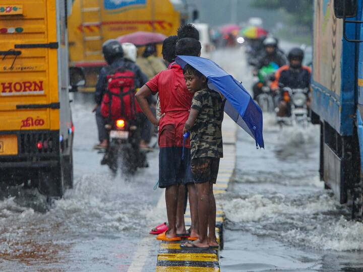 Children holding umbrellas stand on a road divider amid rainfall, in Chennai. In view of the rains, two subways were closed and the city witnessed traffic congestion and slow movement of vehicles. (Source: PTI)