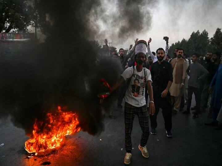 Supporters of former Pakistani prime minister Imran Khan, shout slogans beside burning tyres as they block the main highway near the container truck a day after the assassination attempt on Khan, at the cordoned-off site of a gun attack. (Image Source: AFP)