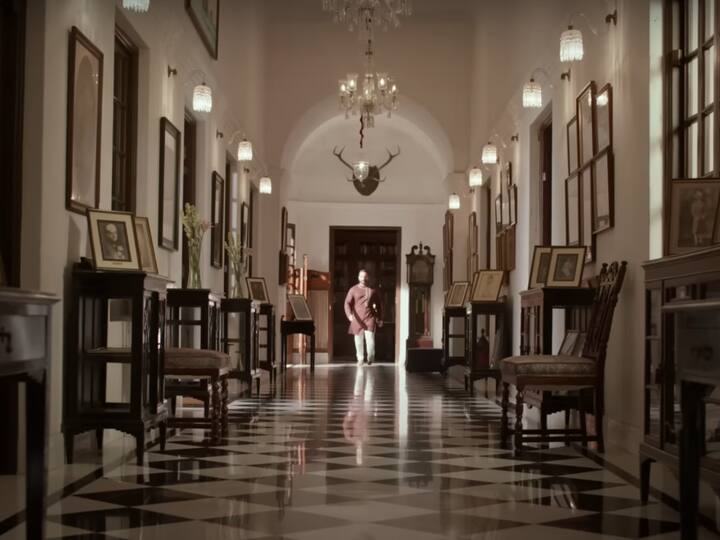 Old paintings, photos, wooden stools, and glass cabinets line both walls of the corridor. With its chessboard-like white and black tiles, the floor is absolutely gorgeous. The palace is built in an old-fashioned architectural style with lofty ceilings and arches. (Image Source: You Tube/ Myntra)