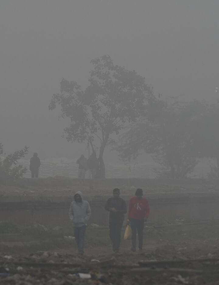 People walk along railway tracks during a cold and foggy morning, in New Delhi. The Safdarjung observatory, Delhi's primary weather station, logged a minimum temperature of 5 degrees Celsius -- three notches below normal. The maximum temperature is likely to settle around 19 degrees Celsius, the weather office said, as per PTI. (PTI Photo/Shahbaz Khan)