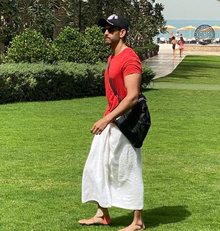 ऋतिक रोशन अपने लुक के साथ एक्सपेरिमेंट करते ही रहते हैं. उनका कम्फर्टेबल स्टाइल स्टेटमेंट इसका सबूत है. इस तस्वीर में ऋतिक ने अपनी प्लेन टी-शर्ट को सफ़ेद स्कर्ट-ईश बॉटम के साथ पेयर किया है. साथ ही ब्लैक कैप और शेड्स वाले सनग्लासेस भी लगाए हैं. लेकिन जो चीज सबसे ज्यादा लाइमलाइट चुराती है, वह है उनका ब्लैक स्लिंग बैग. (इंस्टाग्राम/hrithikroshan)