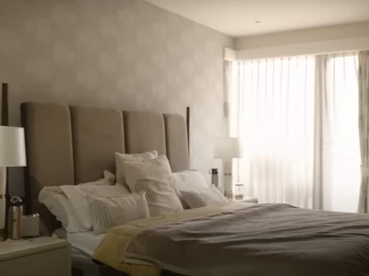Ashneer and Madhuri's bedroom, done in a soothing grey, with a large French window that lets in plenty of light. In addition to their king-sized bed, there are bedside tables packed with 'healthy snacks,' which were formerly filled with chips, according to Madhuri. Both Ashneer and Madhuri enjoy midnight snacking while binge watching on various OTT platforms. (Image Source: YouTube/ Brut India)