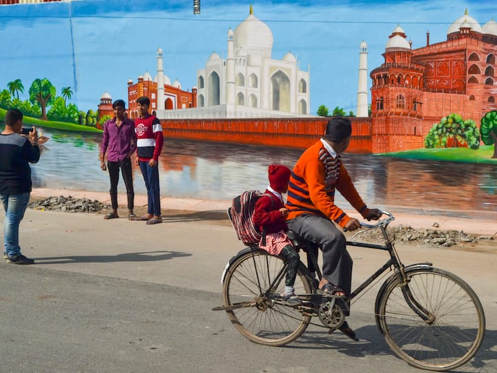 A cyclist passes by the people indulged in clicking pictures in front of a decorated roadside wall ahead of the G20 meeting in Agra on February 13. (Source: PTI)
