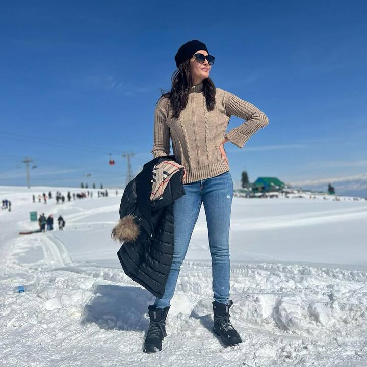 Karishma Tanna poses in a beige top and blue jeans which she has paired with boots, a wooly cap and shades. (Image Source: Instagram)