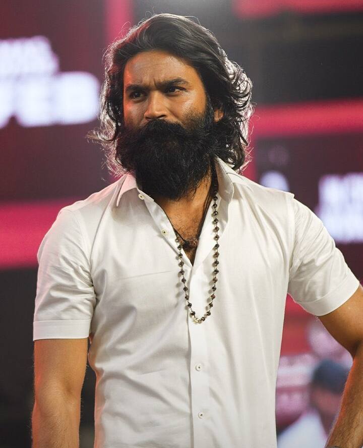 பெரிய தாடி, வளர்ந்த மீசை, நீளமான கூந்தலுடன் சுற்றி வரும் தனுஷின் புகைப்படம்.
