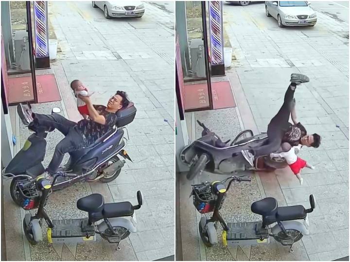 Man lying on a scooty is seen trying to save his child while falling बैलेंस बिगड़ते ही जमीन पर गिरा स्कूटी पर लेटा पिता, समय रहते बचाई बेटे की जिंदगी