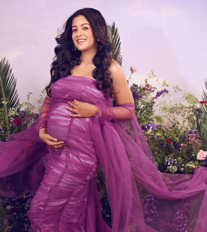 The actor is pictured seated in a flowery scene while wearing a lavender off-shoulder gown.