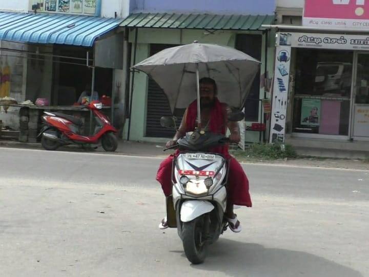 Gurukkal set up umbrellas for shade for two-wheelers in Karur area TNN குடைக்குள் குருக்கள்...வெயிலில் இருந்து தப்பிக்க நல்ல ஐடியா - கரூரில் சுற்றும் ஸ்கூட்டி