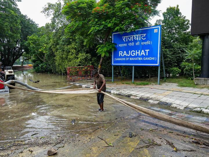 A worker prepares to clear water from a flooded area outside Rajghat due to waterlogging. Image Source: PTI