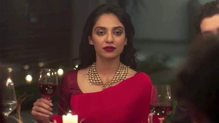 2. Striking red saree:  As Tara, Sobhita donned a striking red saree that accentuated her features and perfectly complemented her skin tone. The ensemble was paired with gold statement earrings and a matching bangle, adding to the overall aesthetic of the outfit. Her hair was styled in loose waves, cascading down her shoulders, and her makeup was kept simple yet glamorous, with a bold red lip that tied the entire look together, and made a saratorial statement for young women.