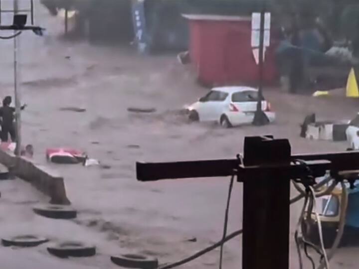People stand on a higher platform to keep themselves safe from the gushing water as vehicles stay submerged during the flood triggered by heavy rainfall in Junagadh. (Image Source: PTI)