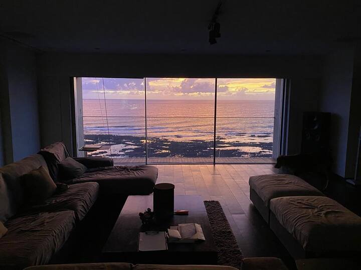 जॉन के इस लग्जरी होम से समुद्र का खूबसूरत नजारा दिखाई देता है. जो घर को एक अलग ही वाइब देता है. ये घर का लिविंग रूम है. जहां कांच का दरवाजा और लाइट ब्राउन सोफे लगे है.