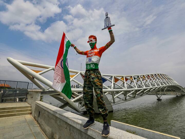 A man painted in the Indian tricolour holds the national flag and a cardboard cutout of Chandrayaan 3 near Atal Bridge in Ahmedabad. (Image Source: PTI)