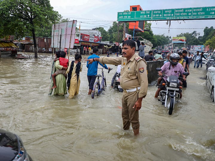 People wade through a waterlogged road in Uttar Pradesh’s Barabanki district after heavy rainfall. (Source: PTI)
