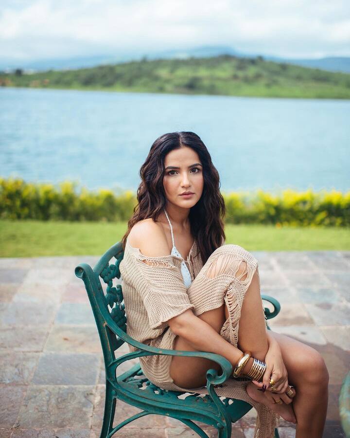 She looks stunning as she poses in the mesh outfit in front of a picturesque background.