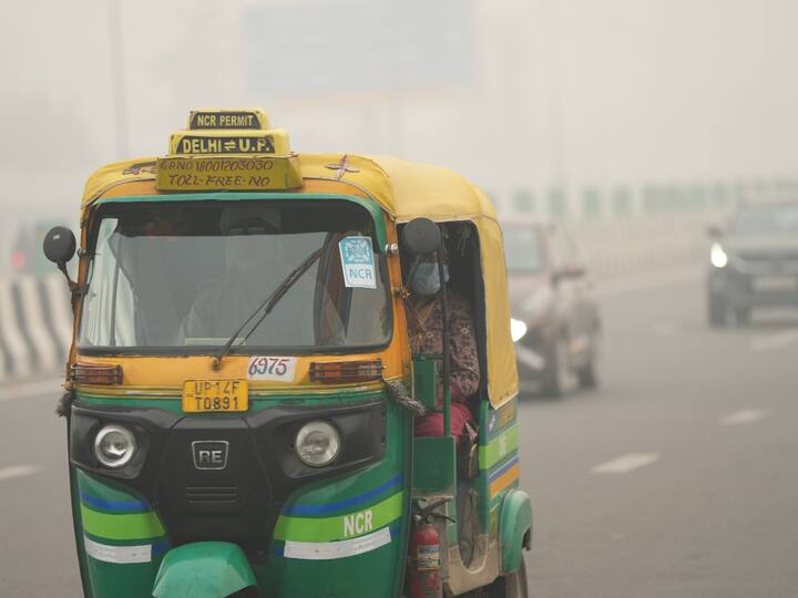An auto rickshaw moves on a Delhi road with a passenger wearing a mask seen on a hazy morning. (Source: PTI)