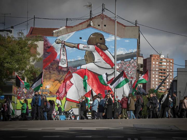 A group of pro-Palestinian protesters pass a mural in Spain's Madrid amid assaults by Israel in the Gaza Strip. Image Source: Getty Images