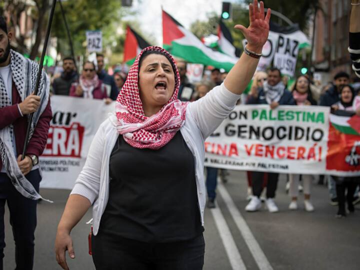 A woman raises her arms during a pro-Palestinian demonstration at the Madrid working-class neighborhood of Vallecas. The Israeli airstrikes have killed more than 9,000 Palestinians in the Gaza Strip including children. Image Source: Getty Images