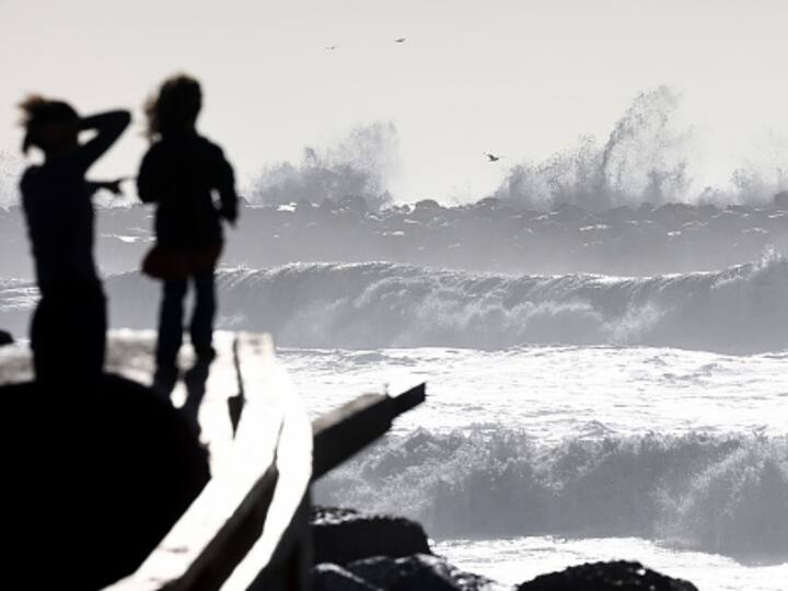 A Pacific Ocean wave crashes against a jetty as other waves roll towards shore with people watching from a playground ship in Ventura. (Image Source: Getty)