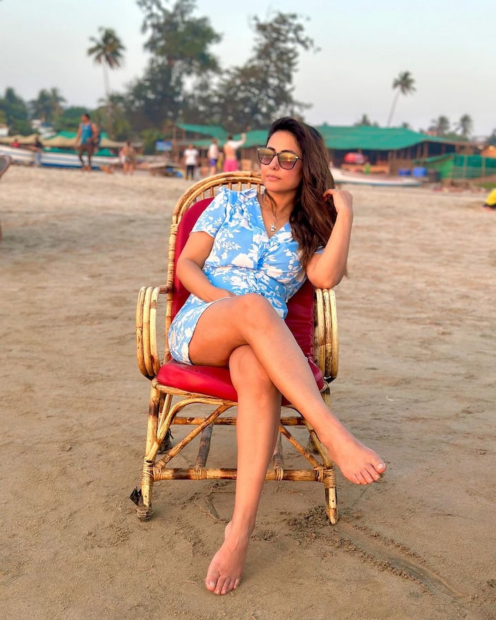 The clicks feature Hina sitting and relaxing in a chair on the beach, wearing a blue short dress, and black sunglasses. She is posing candidly for the lenses while sitting barefooted.