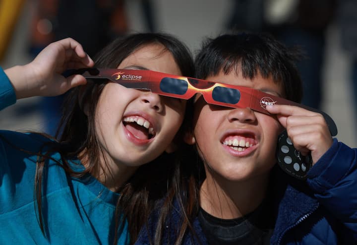 Miriam Toy (L) and Oliver Toy share a pair of eclipse glasses that NASA was handing out as they await the eclipse on April 08, 2024, in Houlton, Maine. (Getty Image)