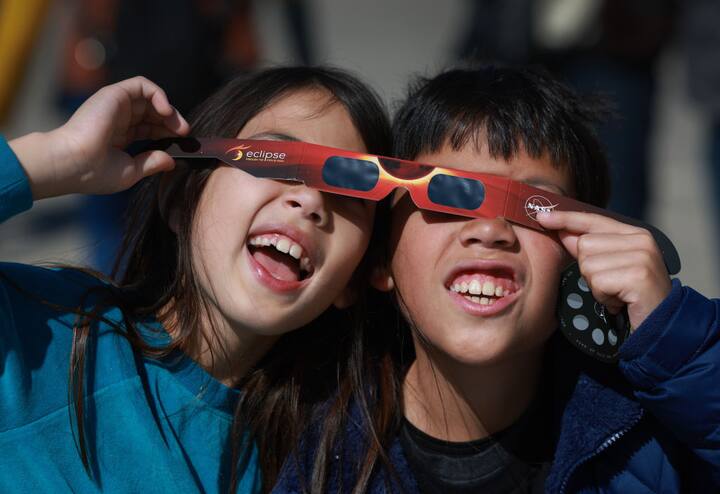 Miriam Toy (L) and Oliver Toy share a pair of eclipse glasses that NASA was handing out as they await the eclipse on April 08, 2024, in Houlton, Maine. (Getty Image)