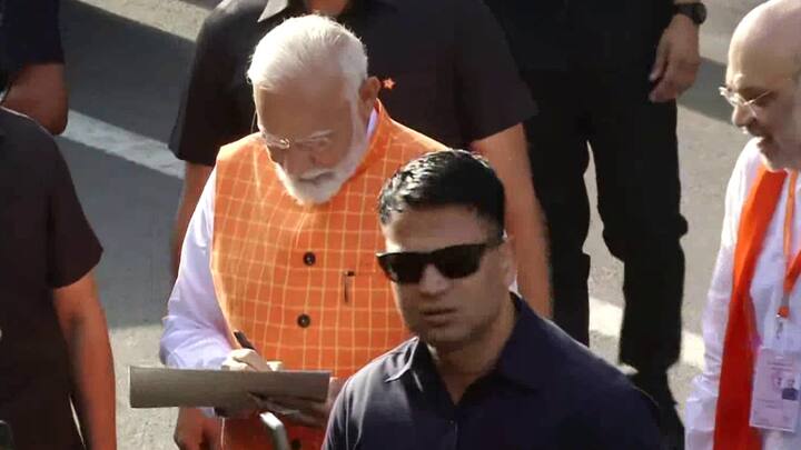 अहमदाबाद के रानिप में मतदान केंद्र पर जुटी भीड़ से बातचीत करते हुए पीएम मोदी ने एक तस्वीर पर हस्ताक्षर किए. मतदान केंद्र पर जाते समय पीएम मोदी ने लोगों का अभिवादन किया. (फोटोः एएनआई)