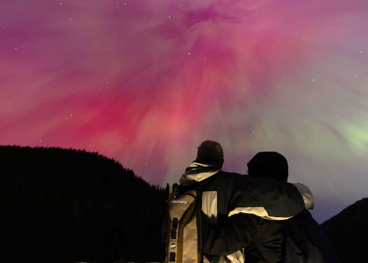 A couple watch the aurora borealis, commonly known as the northern lights on May 11, 2024 in Manning Park, British Columbia, Canada. The spectacle is a result of coronal mass ejections (CMEs) emanating from a colossal sunspot cluster, 17 times wider than Earth. (Source: Getty Images)