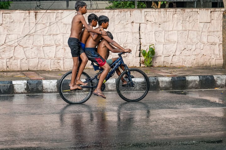 बुधवार, 29 मई, 2024 को नई दिल्ली में गर्मी के एक दिन में थोड़ी सी बारिश के दौरान साइकिल चलाते बच्चे। (स्रोत: पीटीआई)