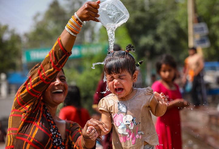 जम्मू में बुधवार, 22 मई, 2024 को भीषण गर्मी के दिन एक महिला चिलचिलाती धूप से राहत के लिए एक बच्चे पर पानी डालती हुई। (स्रोत: पीटीआई)