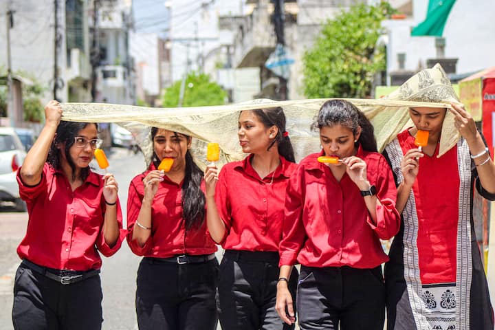 गर्मी के दिनों में चिलचिलाती धूप से राहत पाने के लिए युवतियां अपने सिर को दुपट्टे से ढकती हैं और आइसक्रीम खाती हैं, बुधवार, 29 मई, 2024. (स्रोत: पीटीआई)