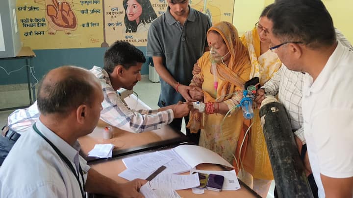 हिमाचल प्रदेश के चुवारी मतदान केंद्र पर लोकसभा चुनाव के अंतिम चरण के दौरान ऑक्सीजन सिलेंडर के साथ वोट डालने पहुंचीं विमला शर्मा नामक महिला (फोटो: @ECISVEEP)