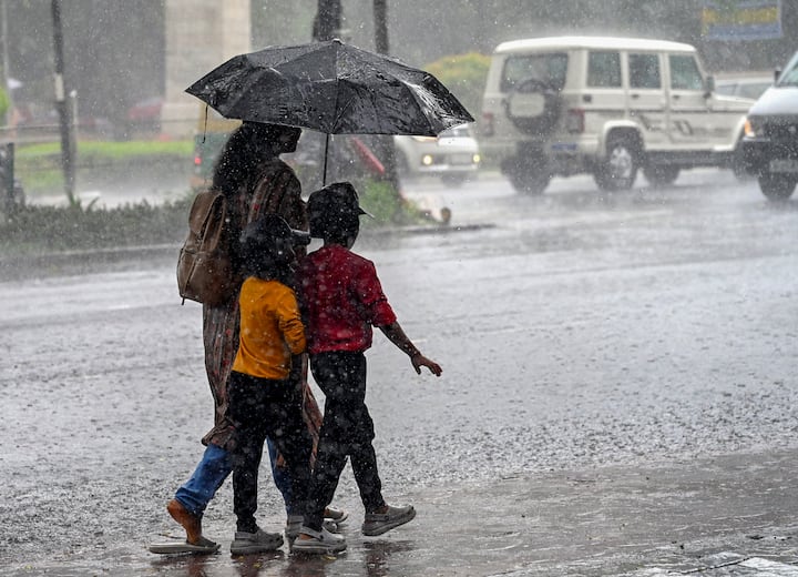 सोमवार, 24 जून, 2024 को तिरुवनंतपुरम में बारिश के दौरान खुद को और अपने बच्चों को बचाने के लिए एक महिला छाते का इस्तेमाल करती हुई। (छवि स्रोत: पीटीआई)