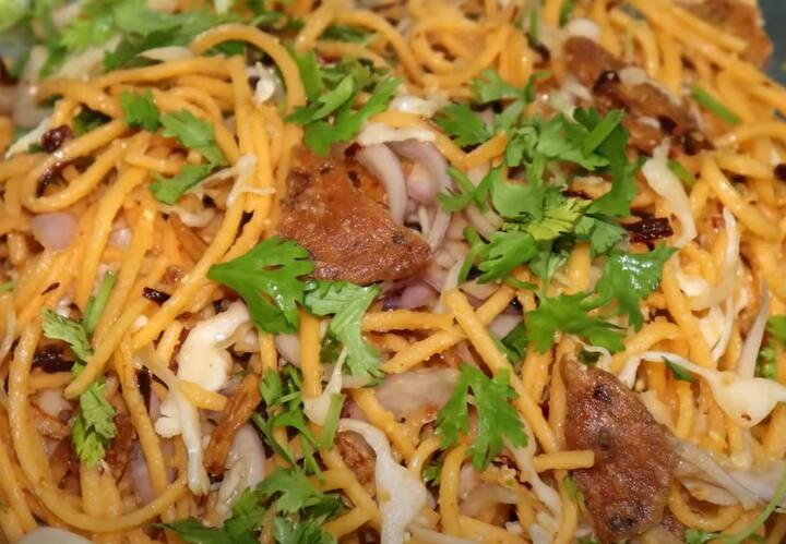 அடுத்தது, ஒரு பாத்திரத்தில் வேக வைத்த நூடுல்ஸ், பெரிய வெங்காயம், முட்டைகோஸ், கேரட், எலுமிச்சை சாறு, புளிச்சாறு, வரமிளகாய் பிளேக்ஸ், தேவையான அளவு உப்பு கலந்த தண்ணீர், தட்டு வடை, கொத்தமல்லி இலை, பொறித்த பூண்டு, பொறித்த வெங்காயம் சேர்த்து கொள்ளவும்.