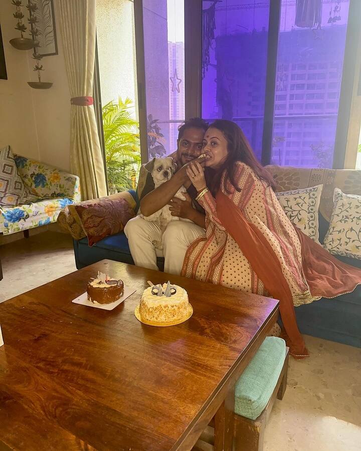 देवोलिना भट्टाचार्जी अपने घर के लिविंग रूम में अपने पति के साथ बैठी हैं. सामने टेबल पर एक्ट्रेस के दो बर्थडे केक रखे हैं.