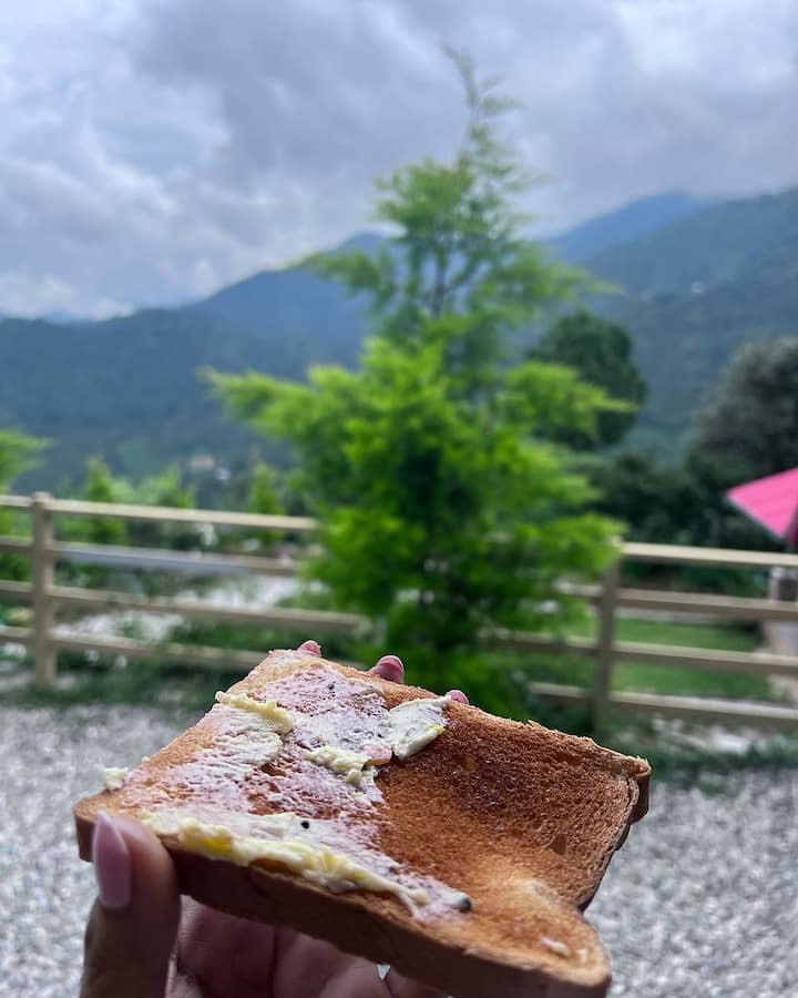 आशा नेगी ने पहाड़ियों में अपनी सहजता की झलकियाँ साझा कीं एक और रमणीय छवि में आशा को पहाड़ों की आश्चर्यजनक पृष्ठभूमि के सामने ब्रेड और मक्खन के सरल लेकिन संतोषजनक भोजन का स्वाद लेते हुए दिखाया गया है।