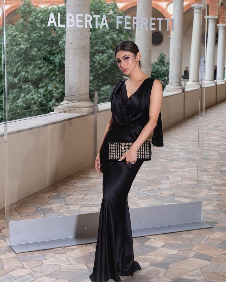 Mouni Roy stunned in a black satin gown with a cowl neck, complemented by a matching trench and elegant makeup.