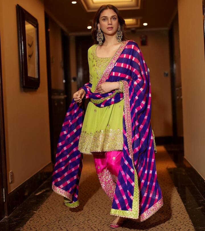 This graceful peacock-green suit, paired with a bright pink-colored salwar, is a vibrant and eye-catching set. The multi-stone cluster drop jhumkas and traditional juttis add to the outfit's ethnic charm, creating an effortlessly elegant and timeless look.