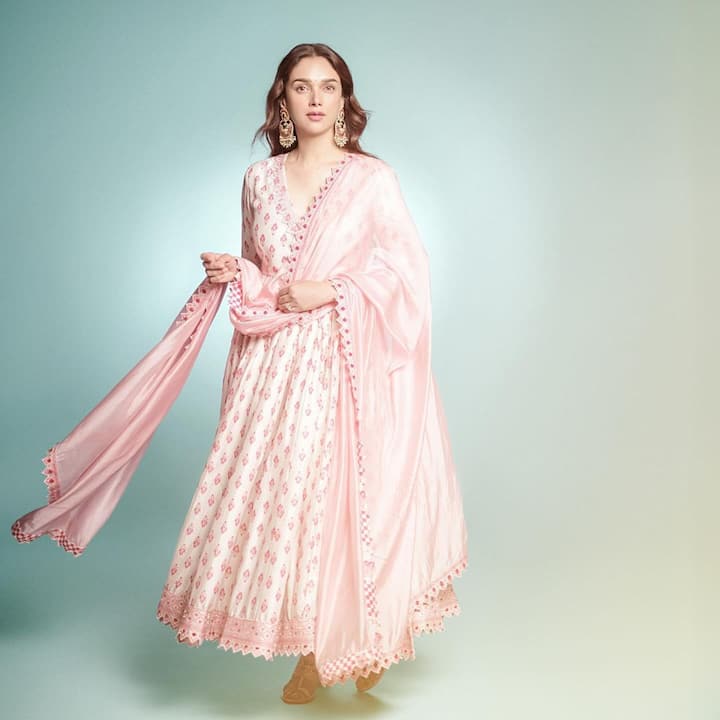 This delicate baby pink ensemble is complemented by subtle nude makeup, perfectly pairing with accessories like a cocktail ring and elegant trendsetting earrings. The standout emerald and multicolored earrings, featuring intricate detailing, add a vibrant pop to the look, enhancing its chic and modern appeal.