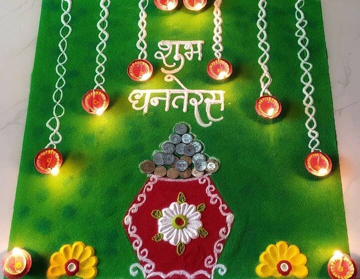 स्क्वायर शेप रंगोली में इस तरीके का पैटर्न भी बहुत खूबसूरत लगता है. आप ग्रीन कलर से स्क्वायर शेप बनाएं, बीच में कलश बनाएं, असली सिक्के उसके ऊपर सजाएं और ऊपर से व्हाइट कलर की स्ट्रिंग्स बनाकर दीये जलाएं और शुभ धनतेरस लिखें.